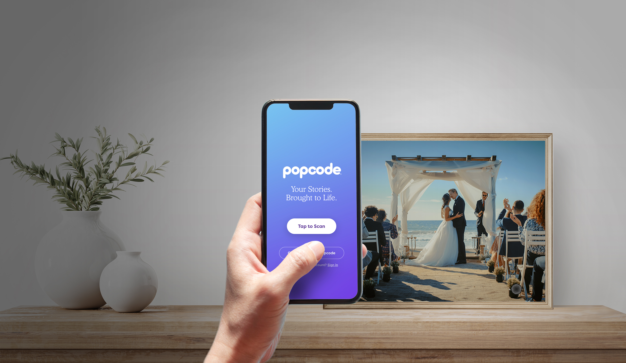 Hand holding phone showing Popcode app next to a framed wedding photo